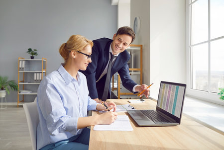 Young business people company employees having discussion about financial data analyzing company accounting on meeting. Woman accountant working on laptop with charts and talking with colleague.の写真素材