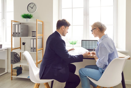 Financial accountant or businessman and his female assistant or colleague sitting at desk, using laptop, looking through financial documents. Two company employees working together with data lists.の写真素材