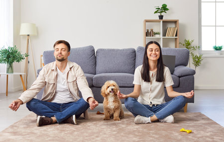 Happy family couple meditates together while practicing yoga with dog at home. The couple enjoys a peaceful domestic life with pet, bonding through relaxation and mindfulness exercises.の写真素材