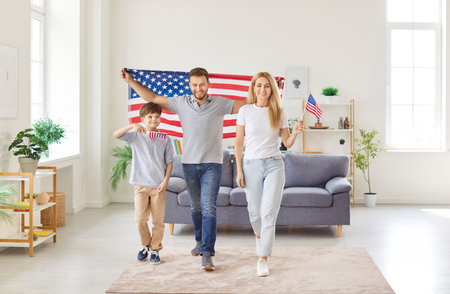 Portrait of a young happy american family with little child boy standing in living room at home with flag of united states celebrating Independence Day. Patriotic US holiday and patriotism concept.の写真素材