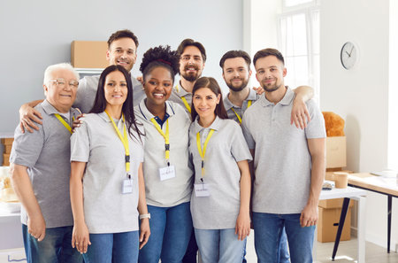 Diverse team of volunteers. Group of happy Caucasian and African American people in gray uniform T shirts with ID tags in a small food aid storehouse. Charity work, non profit organizations conceptの写真素材