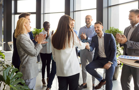 Business people introduce new female employee worker on group meeting in modern office, welcome newcomer at workplace, colleagues applauding congratulating recruit with job promote, agreement dealの写真素材