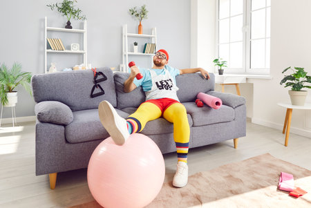 Funny happy sportsman relaxing pose doing body rest on sofa, exercise dumbbell, playful fitness comedian, sporty humorist, fit clown in amusing sportswear, athlete health enthusiast, fitness freakの写真素材