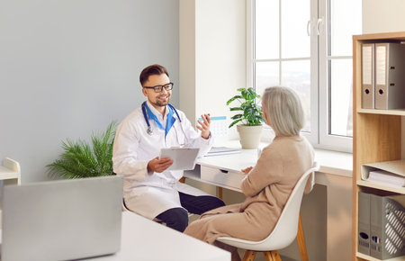 Positive doctor or nurse is talking to an elderly patient during a hospital visit. The medical professional is providing healthcare and therapy, engaging in a conversation with the patient.の写真素材