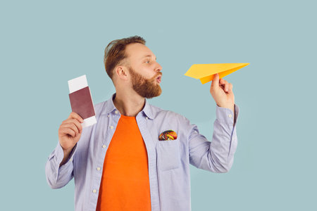 Portrait of a young happy man tourist in casual clothes holding boarding pass with passport and paper plane ready for summer holiday trip. Vacation, journey and travelling concept.の写真素材