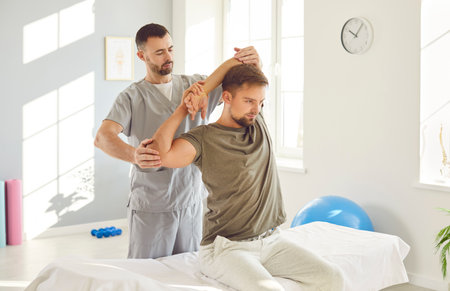 Therapist performing massage and stretching arm joints exercises to aid in the patient recovery. This physiotherapy and rehabilitation session improving joint mobility and promote medical healing.の写真素材