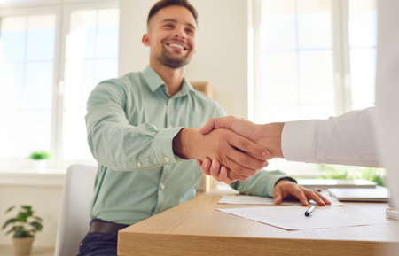 Happy smiling man shaking hands with his partner sitting at workplace in office celebrating success, making a good deal, business achievement, signing a contract or greeting new employee.の写真素材