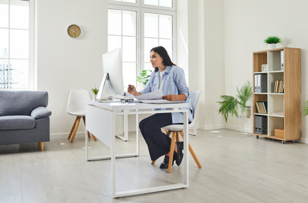 Female financial accountant, bookkeeper, auditor or secretary working on her computer in the office. Young woman sitting at her desk, working with documents and using a modern computerの写真素材