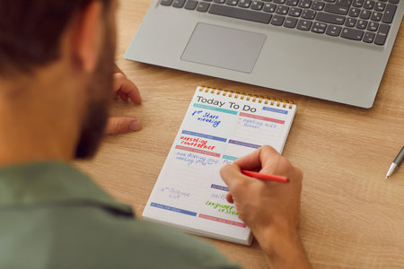 Top view of businessman planning tasks and to do list in his notepad sitting at desk with laptop at home or at office. Man looking to schedule calendar with daily plans. Business planner concept.の写真素材