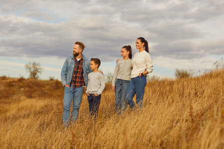 Portrait of happy smiling young family with son and daughter standing outdoors enjoying beautiful nature in the field. Mother, father with two kids hiking together. Family leisure concept.の写真素材