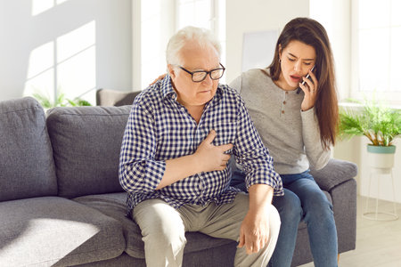 Senior man old father clutches chest in pain heart attack daughter calling to emergency. Daughter calling by phone to emergency senior father heart attack stressing cardiac problem heart attackの写真素材