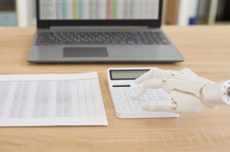 Robotic hand, mechanical arm on calculator, accounting machining processes, laptop screen checking stock market data, AI-powered accounting software trading stocks information for growth, profitの写真素材