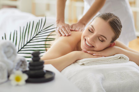 Therapist performs back massage for smiling woman in spa salon, providing therapy and body care in a professional setting with focus on treatment and wellness in a comforting space.の写真素材