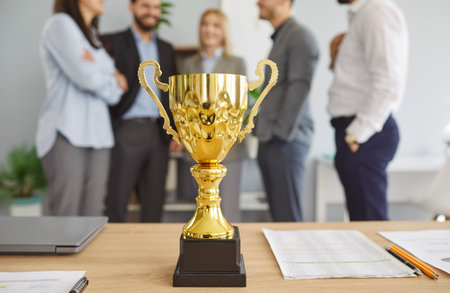 Golden and shiny champion cup on table with business people team in office background, celebrating success, achievement, and victory with award in a professional setting with pride.の写真素材