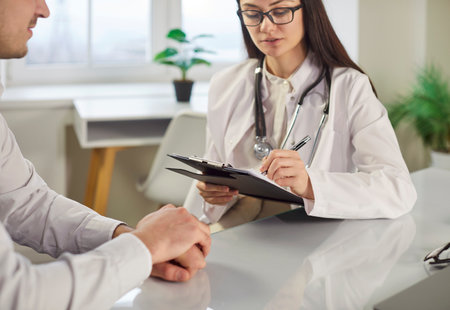 Female doctor holding medical appointment, listening to man patient complaints, offering care and support, providing professional consultation, giving recommendations, posing in hospital officeの写真素材