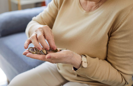 Cropped portrait of poor old senior woman sitting on couch in the living room at home and counting coins in hands. Elderly person holding money in palms. Pension poverty and savings concept.の写真素材