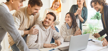 Group of happy college university students celebrating successful launch of digital online project. Team of smiling young adult friends in classroom with laptop computer. Education technology conceptの写真素材