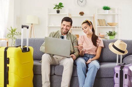 Newlywed couple planning their honeymoon trip, comparing prices on website while choosing tour online, enjoying summer holidays, posing on sofa with packed suitcase around. Travel conceptの写真素材