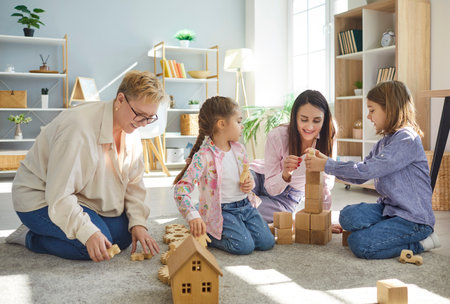 Loving senior grandmother, mother playing, construct with wooden blocks bricks granddaughter, grandson sitting on floor grandma baby sitter with kid girl, boy with cute children, preschool grandchildの写真素材