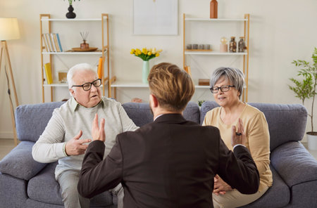 Male financial advisor having discussion with elderly man and woman couple who are sitting on sofa, receiving advice about health insurance. Businessman manager consulting about investment deal termsの写真素材