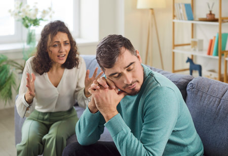 Angry wife shouting in quarrel on her unhappy upset husband sitting on sofa at home. Young couple quarreling and arguing in living room. Marriage problems, relationship and divorce concept.の写真素材