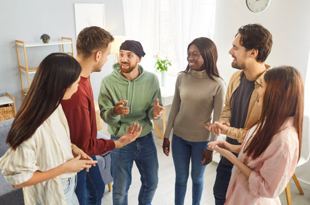 Group of mixed race friends meeting together and having talk, discussing their ideas and plans for startup, standing in half circle, having glad expression, enjoying informal conversationの写真素材