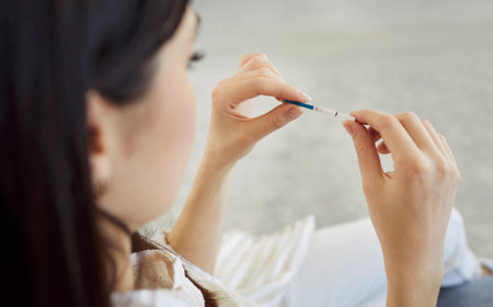 Close up shot showing young woman holding pregnancy test with two red stripes, indicating positive result. Concept of pregnancy, fertility, maternity, family planning and life changing news.の写真素材