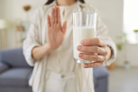 Close up of young woman holding glass of milk and showing refusal gesture with hand. Female person rejecting dairy product due to lactose intolerance, allergy, dietary choice or health concern.の写真素材