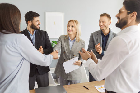 Business people meet for contract negotiation, make a deal, thank each other for collaboration and exchange handshakes. Smiling women shake hands as men applaud. Professional partnership conceptの写真素材