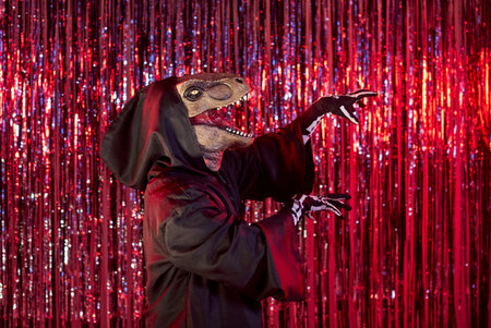 Portrait of person wearing dinosaur mask and black carnival costume with hood having fun and scaring...