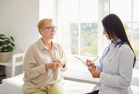 Portrait of a senior elderly woman patient in medical office talking to a female doctor holding report file with appointment and giving consultation during medical examination in clinic.の写真素材