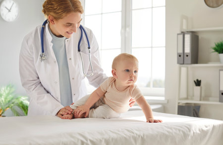 Portrait of young friendly female cheerful pediatrician doctor examining cute little toddler child baby lying on couch in medical clinic. Pediatrics, medicine and children health care concept.の写真素材