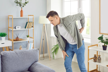 Man at home feeling sudden bad muscles pain attack, holding back, having problem with standing up, suffering from chronic backache, kidney disease, lumbar osteochondrosis, inflammation, rheumatismの写真素材