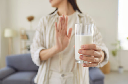 Woman with lactose intolerance or milk allergy holding glass of milk, doing stop gesture, saying no to gastrointestinal problems, sensitivity, dyspepsia, stomachache, bloating reaction. Health conceptの写真素材