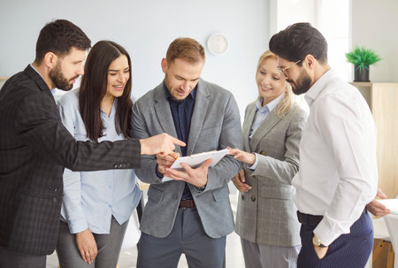 Business group discussing project details, diverse colleagues meet in office, standing share opinion, working on collaborative task, sales manager and company clients checking new paper documentsの写真素材