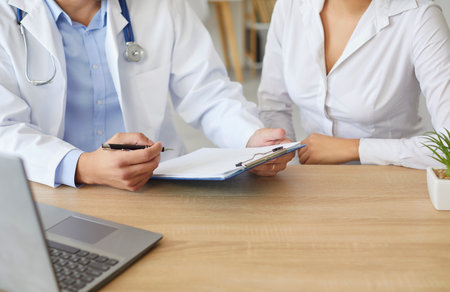 Doctor and patient at desk close up, professional taking notes in journal, physician therapist practitioner filling medical documents, clipboard, patient form, illness history, prescription writingの写真素材