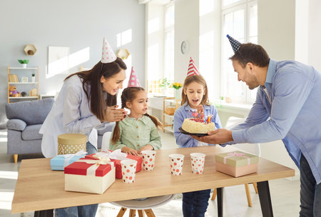 Family happy birthday funny party, overjoyed candid parents and children laughing getting birthday cake, surprise gift, celebrating, enjoying carefree holiday, wearing bright and colourful capsの写真素材