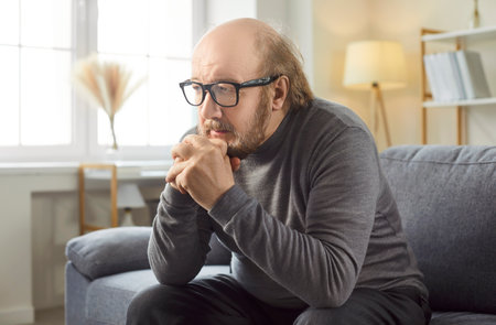 Senior alone unhappy old man sitting on sofa at home, feeling lonely retired grandfather worrying about difficult life, problems, depression, rehabilitation need, pondering, thinking, planningの写真素材