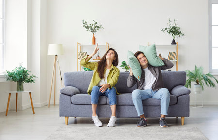 Young couple annoyed by the loud noise from neighbors, covering ears at home. Disturbance caused by renovation, loud music, or other noisy activities in a shared living environment.の写真素材