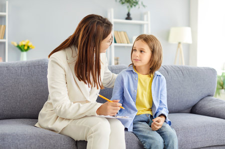 Portrait of a friendly young female psychologist woman doctor supporting her child girl patient sitting on sofa in office during therapy session. Psychotherapy and kids mental health concept.の写真素材