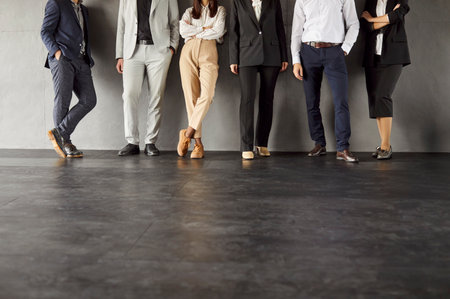 Legs of unrecognizable business people men and women standing in a row in office on gray background. Cropped shot of a group of employees in formal clothes standing on a meeting. Teamwork concept.の写真素材