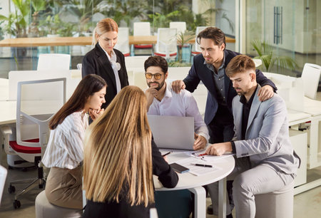 Team of business colleagues sit at round table meet for brainstorming focused at laptop computer, work on project, discussing company finances, study sales date, do paper work togetherの写真素材