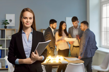 Portrait of a professional businesswoman smiling. Colleagues community working in background in office. Successful and happy people collaborating in a productive business environment.の写真素材