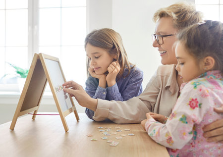 Grandmother teaching her grandchildren to read, using magnetic board and letters, playing spelling game, learning alphabet, making some words. Children, education at home and family leisureの写真素材