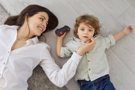 Top view portrait of happy young mother lying on floor in living room at home with cute child boy...