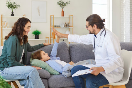 Friendly family pediatrician in medical coat high five giving after checking little boy health, specialist exams small cute patient at health check, pediatry, caring nurse, GP consultation at homeの写真素材