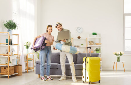 Young family looking for hot sale for summer vacation, booking tickets online for flight, focused at laptop screen, standing in full length in living room, preparing for vacationsの写真素材