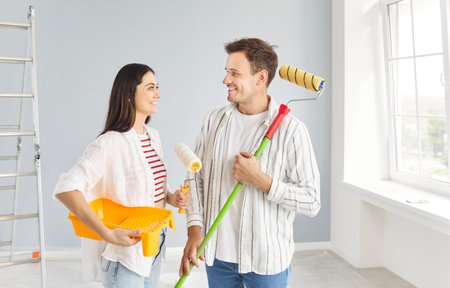 Young couple happy painters planning new flat construction, painting wall with paint roller brush, finishing task for room moving, building repair, remodeling, renovation, starting new life togetherの写真素材