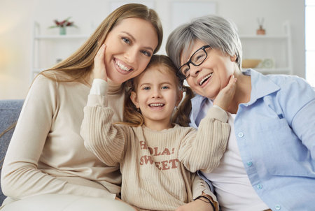 Family portrait of three women generations pose together with happy expressions have good relationships, posing at home. Cheerful small girl poses between her mother and grandmotherの写真素材
