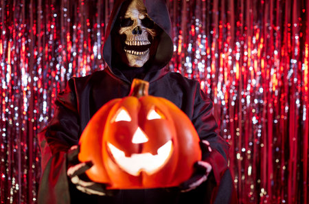 Close-up of grim reaper holding pumpkin during halloween party, featuring skeleton and terrible horror monster in a nightmare setting with mystery and intrigue every moment of the event.の写真素材